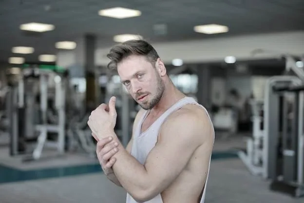 Confident muscular man poses in a modern gym, showcasing strength and fitness.